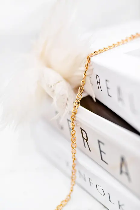 Fine yellow gold mariner or anchor link chain draped diagonally over a stack of white books — stand-in photograph