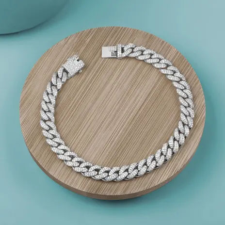 Iced-out white metal Miami Cuban link choker laid in a ring on a pale wooden disc against a teal background — stand-in photograph