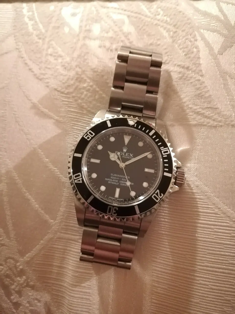 Stainless steel Rolex Submariner ref. 14060M with black dial and bezel, laid flat on cream damask cloth — stand-in photograph